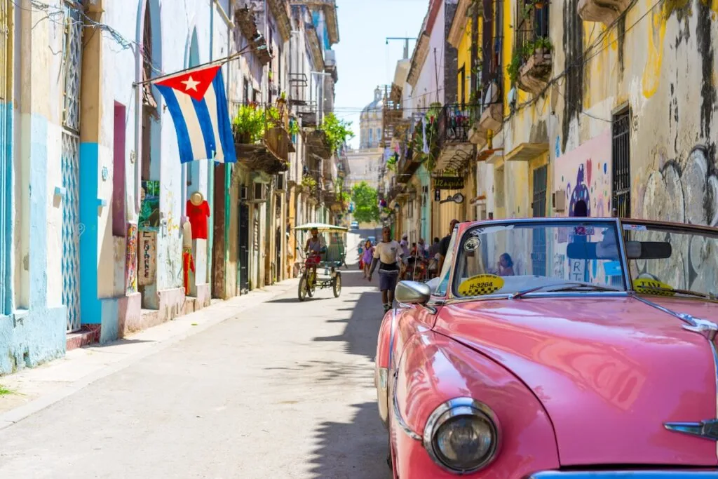 1950's model pink convertible car parked in street in front of weathered yellow and blue buildings in Cuba, pink convertible car photo
