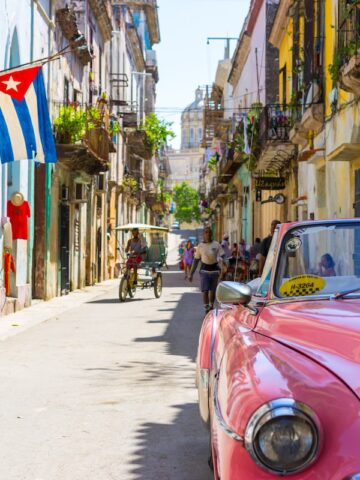 1950's model pink convertible car parked in street in front of weathered yellow and blue buildings in Cuba, pink convertible car photo