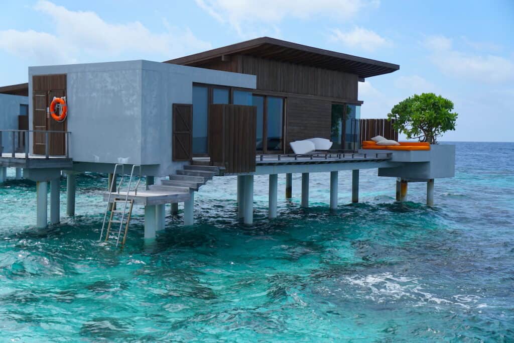 gray and brown building on stilts over turquoise blue water, overwater villa suite in Maldives