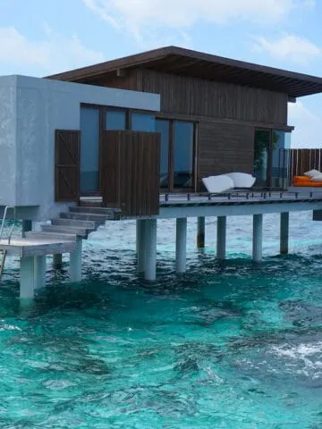 gray and brown building on stilts over turquoise blue water, overwater villa suite in Maldives