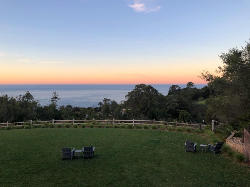 black wood lounge chairs on dark green lawn overlooking sunset over ocean at Alila Ventana Big Sur