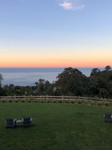 black wood lounge chairs on dark green lawn overlooking sunset over ocean at Alila Ventana Big Sur