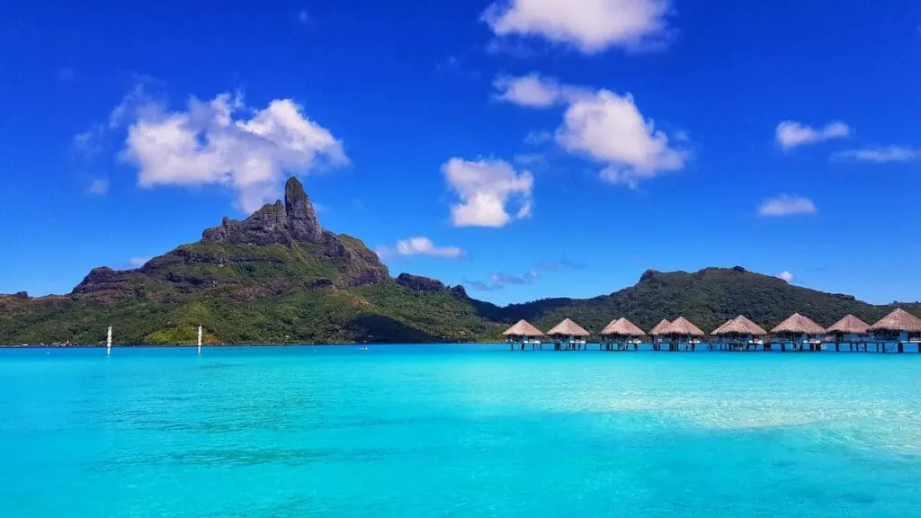 green mountain beside body of water under blue sky during daytime, thatched hut overwater villas, Bora Bora French Polynesia