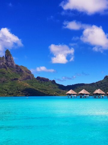 green mountain beside body of water under blue sky during daytime, thatched hut overwater villas, Bora Bora French Polynesia