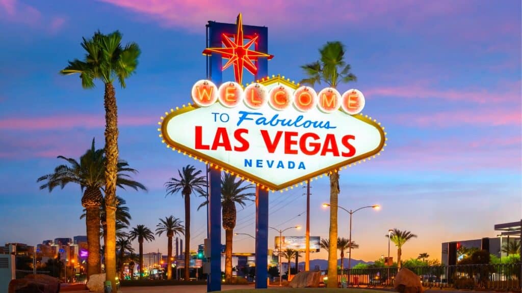colorful neon sign welcoming visitors to Las Vegas flanked by tall palm trees at sunset