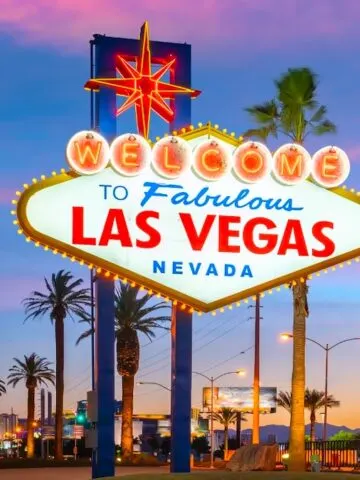 colorful neon sign welcoming visitors to Las Vegas flanked by tall palm trees at sunset