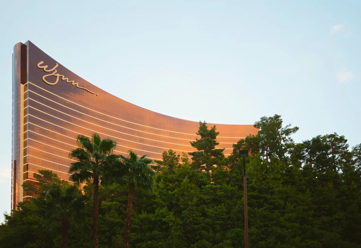 dark green palm trees and tall green trees in front of brown and gold skyscraper building during daytime; wynn las vegas