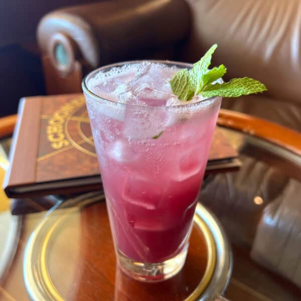 Purple liquid in tall glass with mint garnish on top of round glass table with wood edge