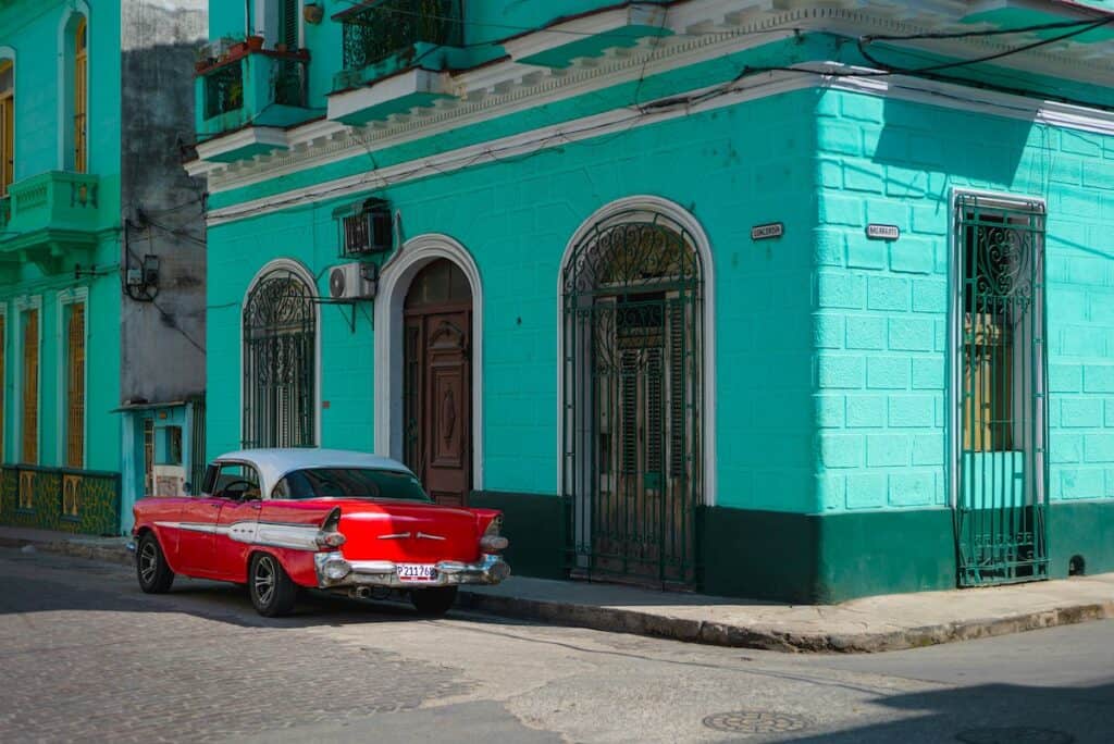 red 1950's coupe with white roof parked beside aquablue concrete building during daytime, Havanna, Cuba
