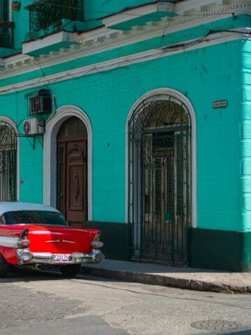 red 1950's coupe with white roof parked beside aquablue concrete building during daytime, Havanna, Cuba