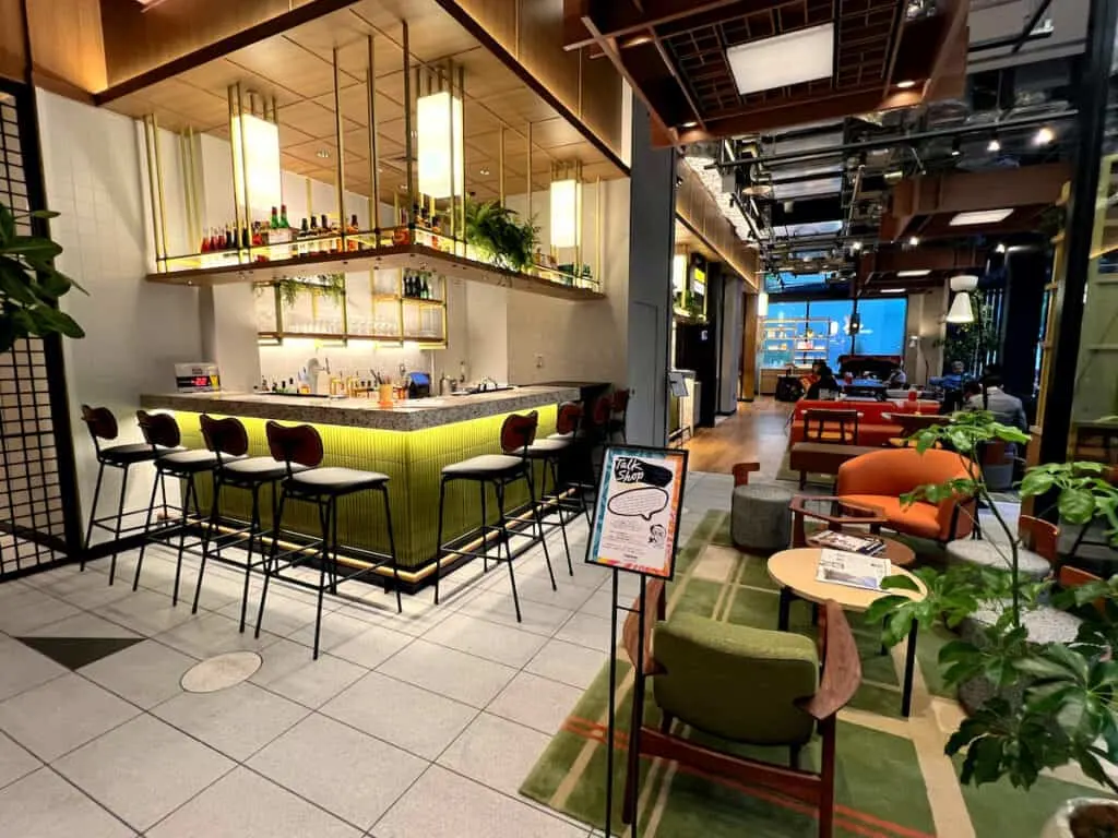 Contemporary marble topped bar with high backed bar stools near across from green and orange chairs on a green and beige rug