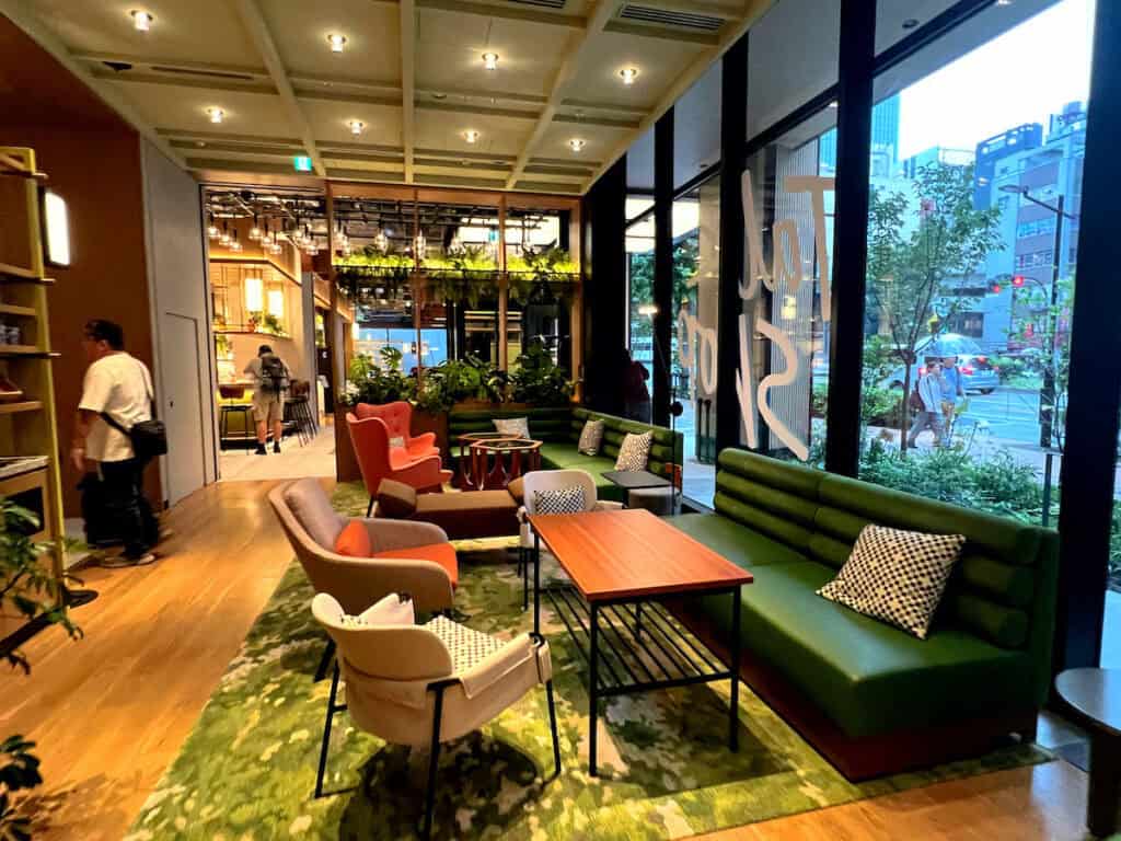 Green sofas, orange high backed chairs, and beige chairs sitting in front of wood tables on green rug i hotel lobby