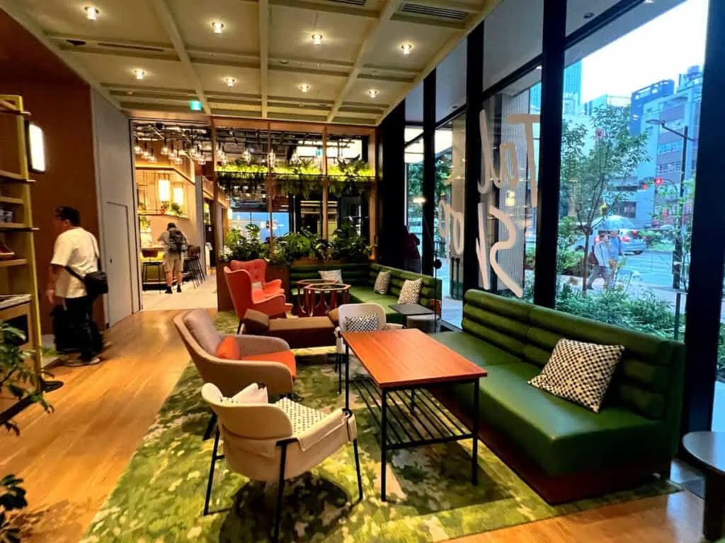 Green sofas, orange high backed chairs, and beige chairs sitting in front of wood tables on green rug i hotel lobby