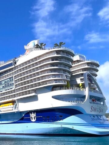 Mega cruise ship painted light blue on the bottome and white on top docked at cruise port on a sunny day with whispy white clouds