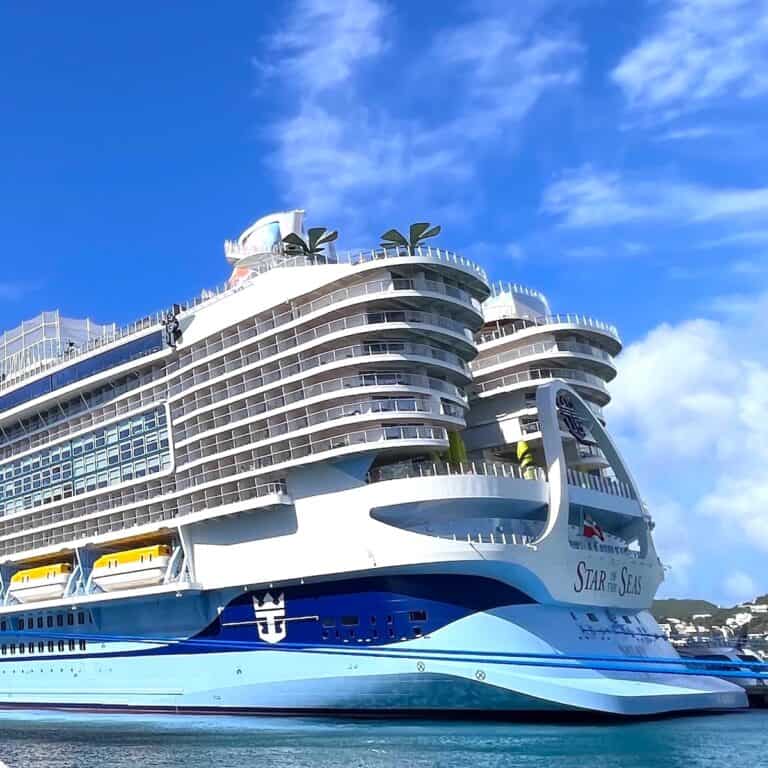 Mega cruise ship painted light blue on the bottome and white on top docked at cruise port on a sunny day with whispy white clouds