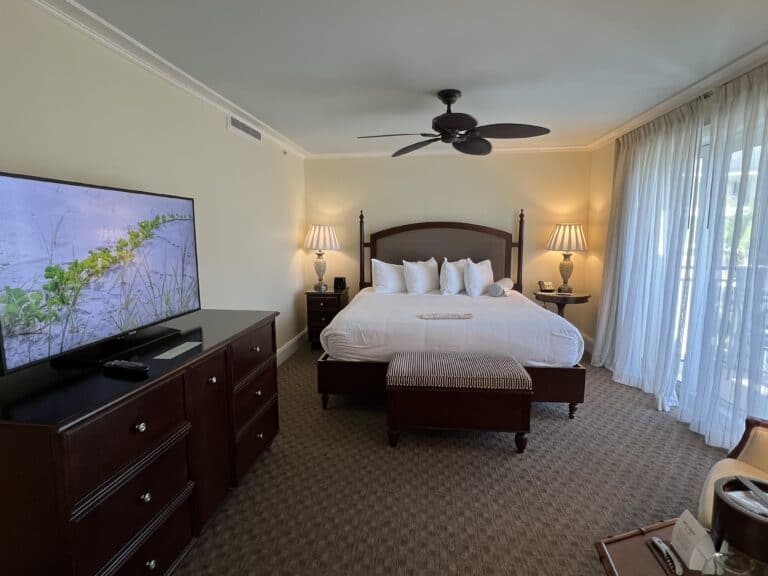 hotel room with brown wooden bed with white sheets, brown ceiling fan, flat screen tv on top of brown dresser