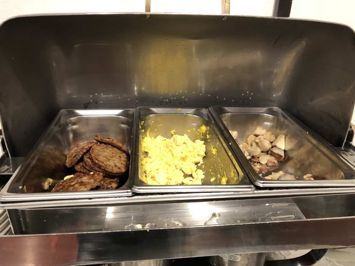 three rectangle silver warming trays holding circular patties of sausage, yellow scrambled eggs, and wedget cut cooked potatoes