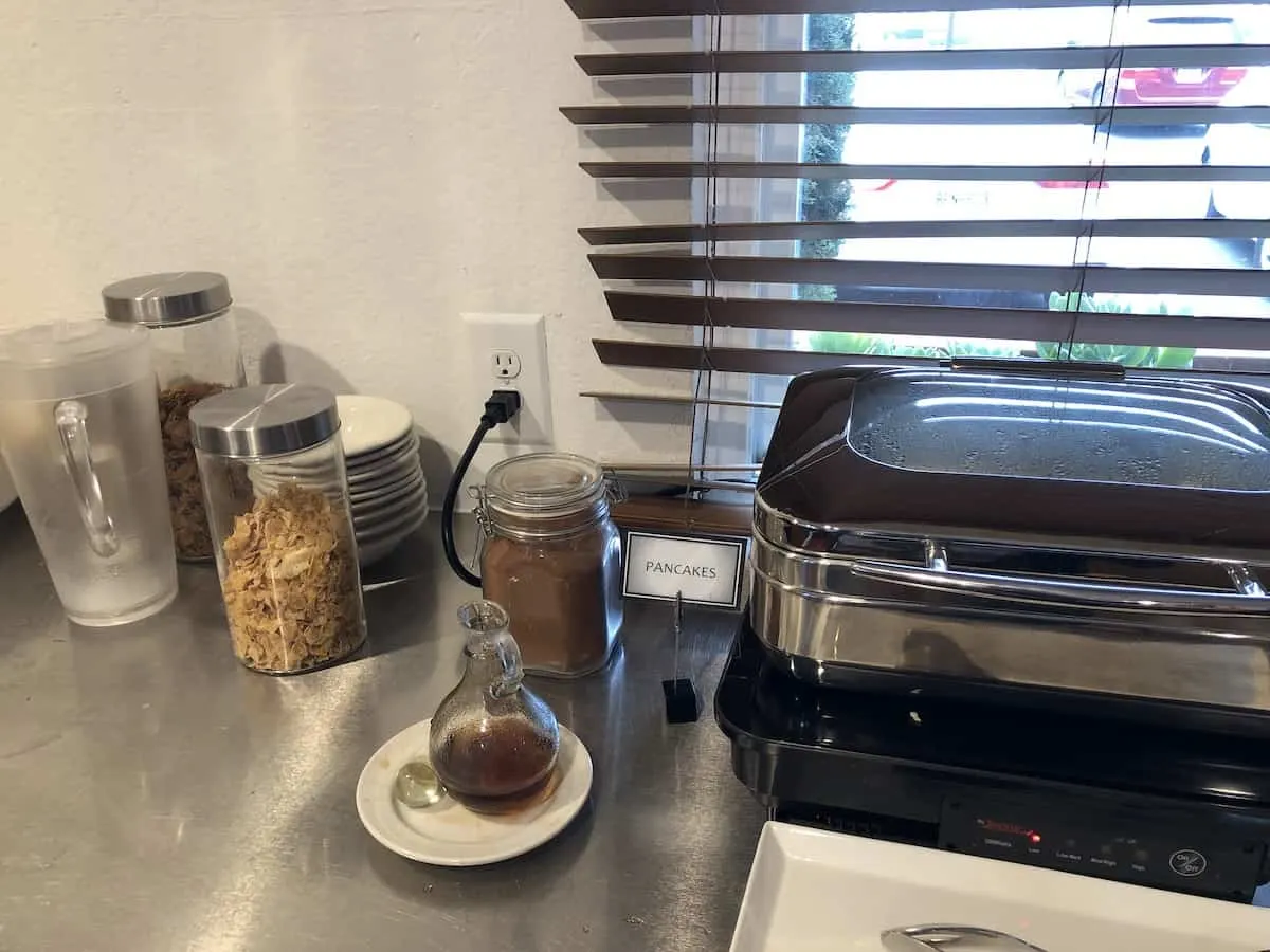 clear container with cereal, black warming tray with pancakes