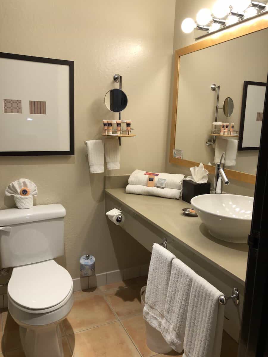 beige bathroom with wood framed mirror, white towels, and orange colored toiletries