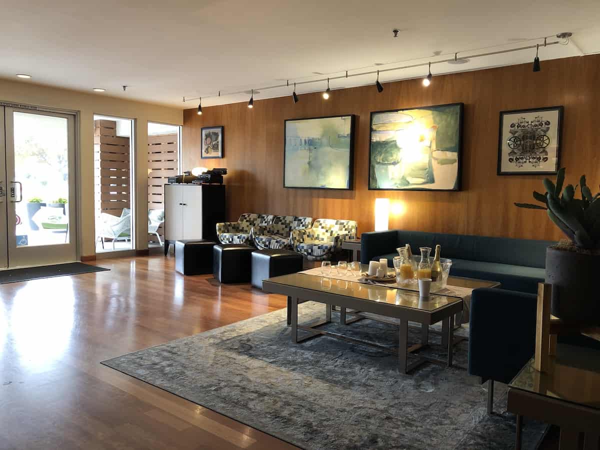 dark teal sofa, three chairs covered in fabric of white, blue gray black squares , glass topped coffee table, cactus, two antique typewriters on cabinet in hotel lobby