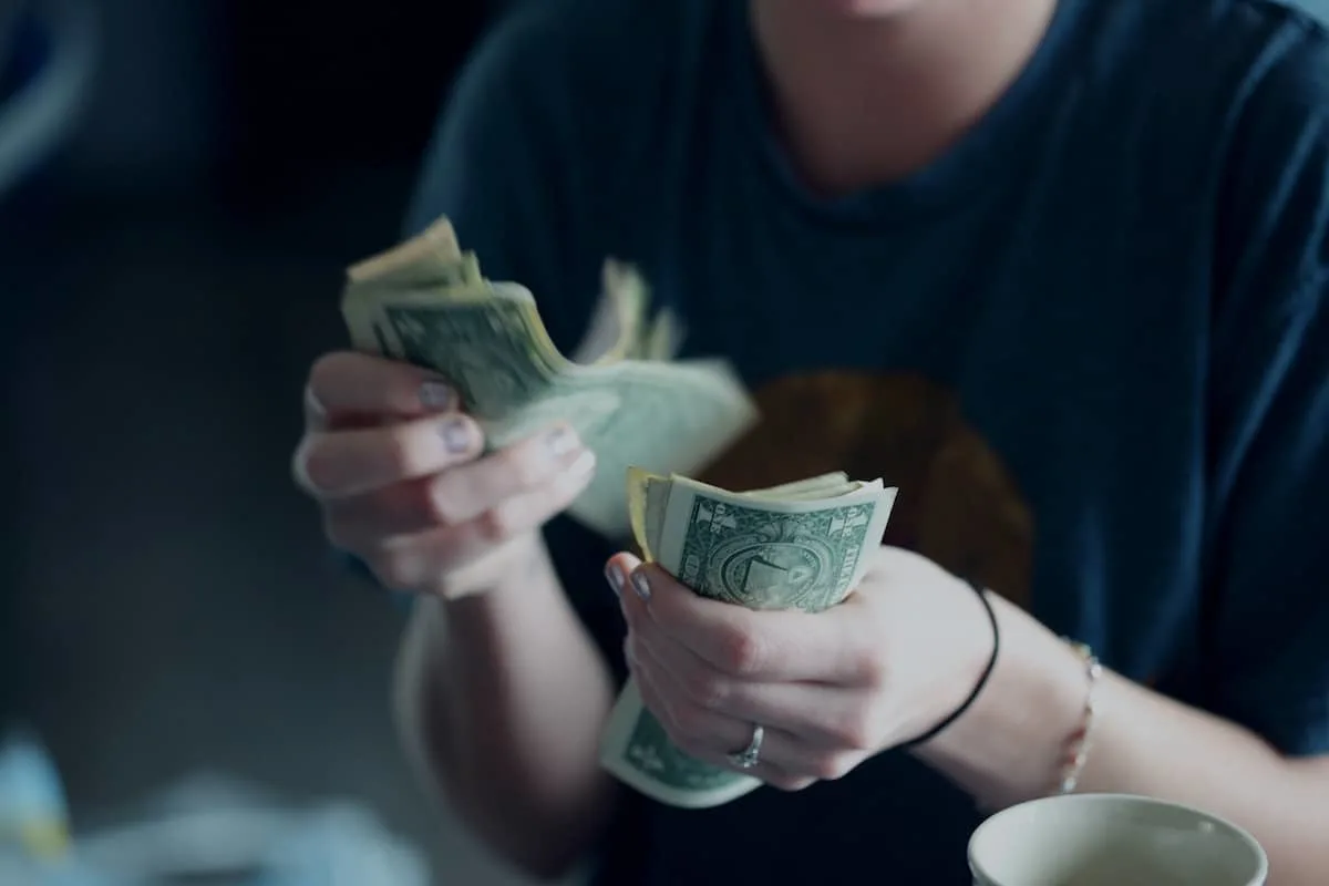 caucasian person in blue shirt with silver nail polish counting dollar bills