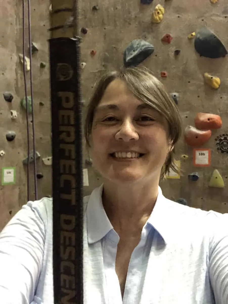 brunette woman in light colored shirt in front of an indoor rock climbing wall